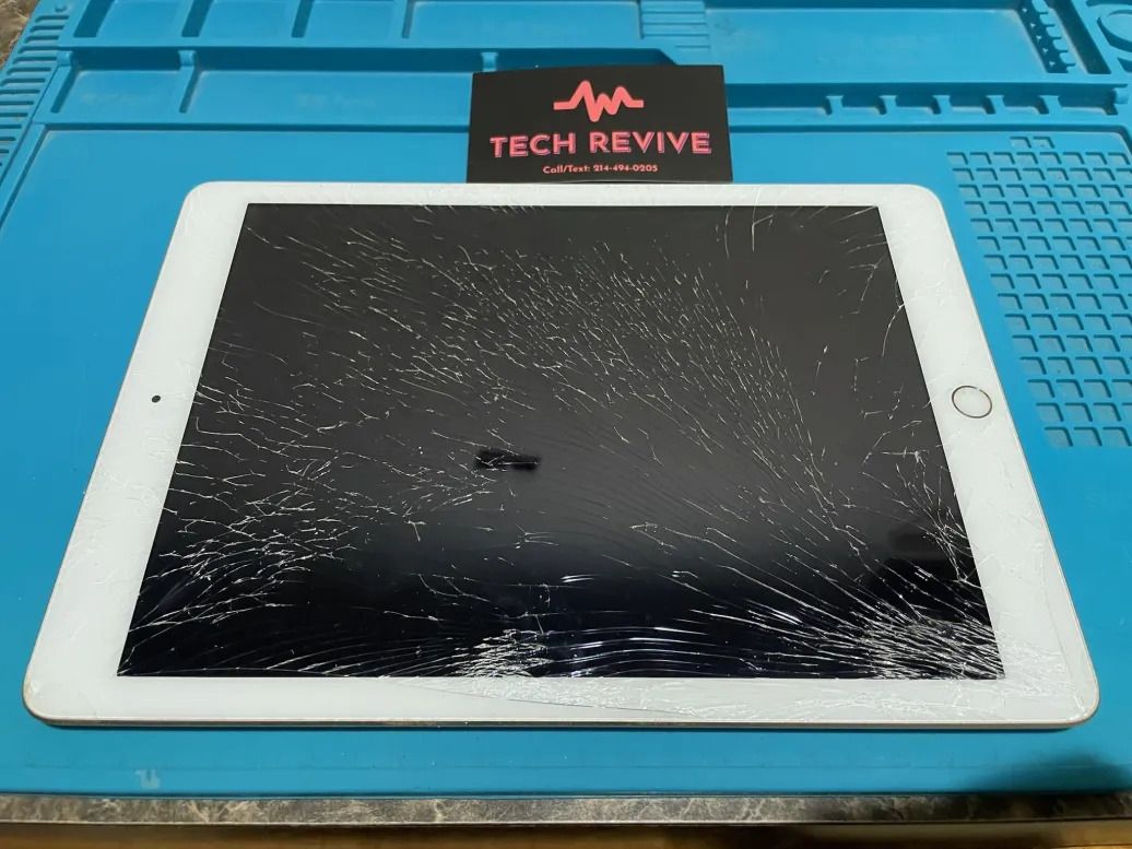 A tablet with a badly cracked screen on a blue repair mat